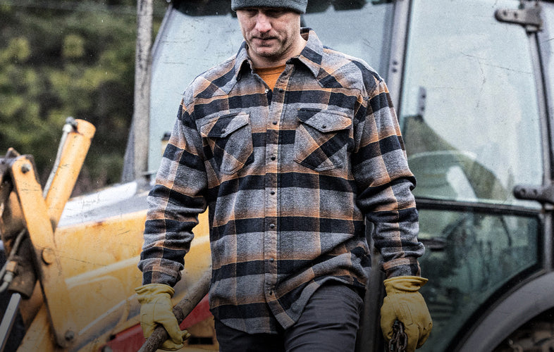 man in flannel shirt and gloves walking in front of heavy machinery