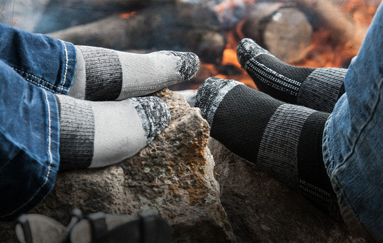 two people without shoes on warming their socks in front of a fire