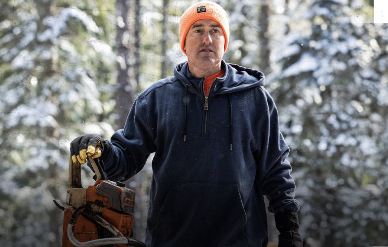 man wearing sweatshirt holding a chainsaw in a snowy forest clearing