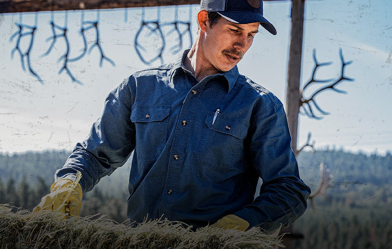 man wearing long sleeve shirt and gloves moving a bail of hay