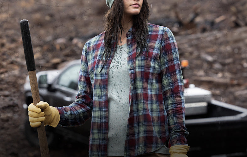 woman with a flannel sweatshirt and hoodie on standing in front of truck on a dirt hill