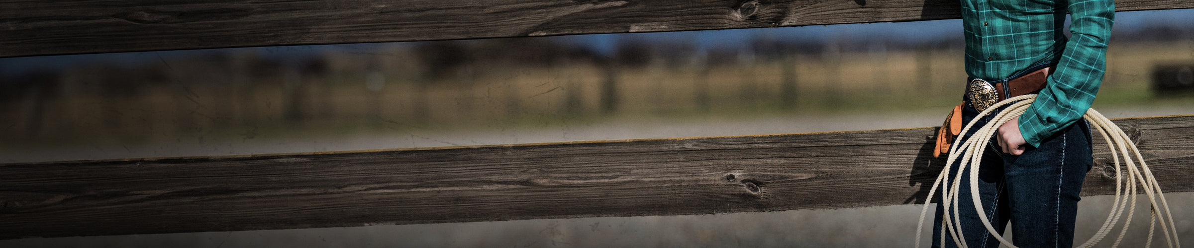 woman with coil of rope and belt buckle standing in front of wooden fence