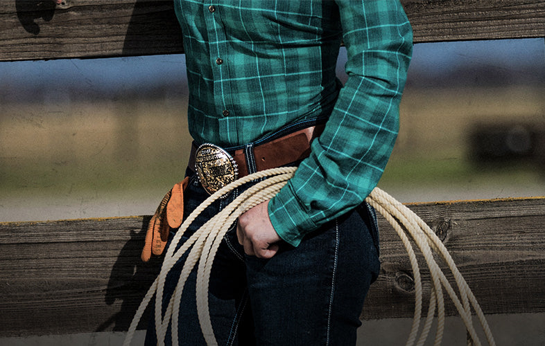 woman with coil of rope and belt buckle standing in front of wooden fence